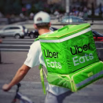 Repartidor con mochila de Uber Eats en bicicleta, asociado a plataformas de entrega y consolidación global.