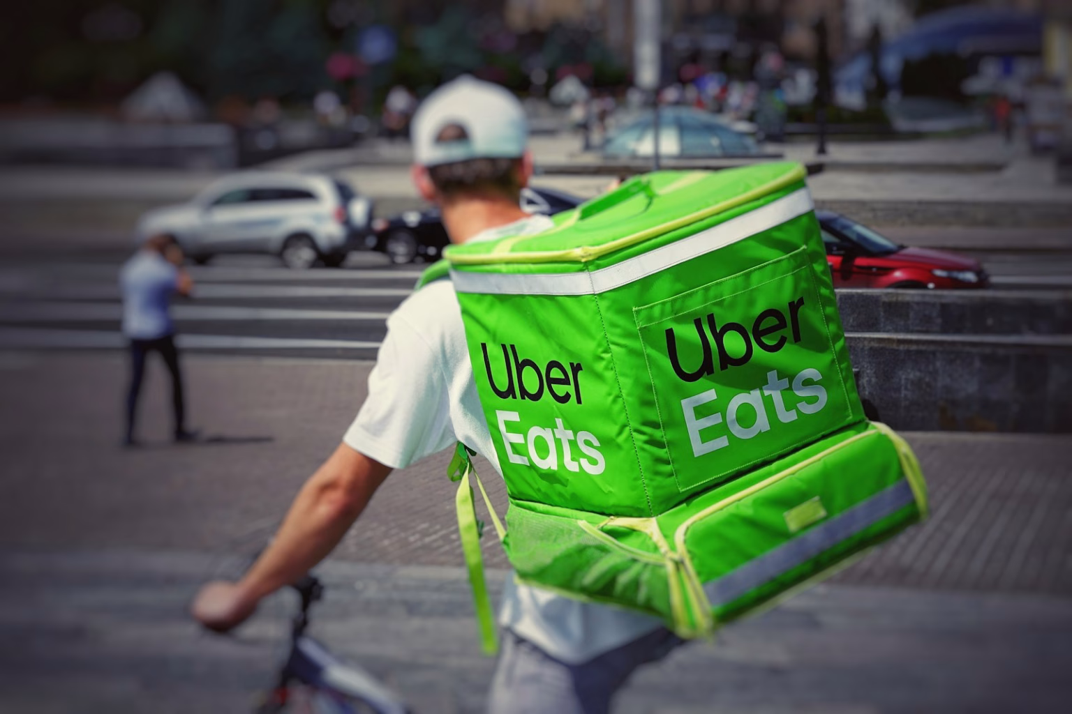 Repartidor con mochila de Uber Eats en bicicleta, asociado a plataformas de entrega y consolidación global.