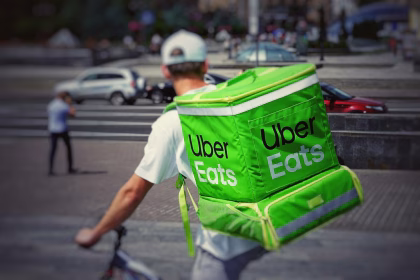 Repartidor con mochila de Uber Eats en bicicleta, asociado a plataformas de entrega y consolidación global.