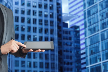 Persona usando una tableta ante edificios para ilustrar negocio de dispositivos tecnológicos