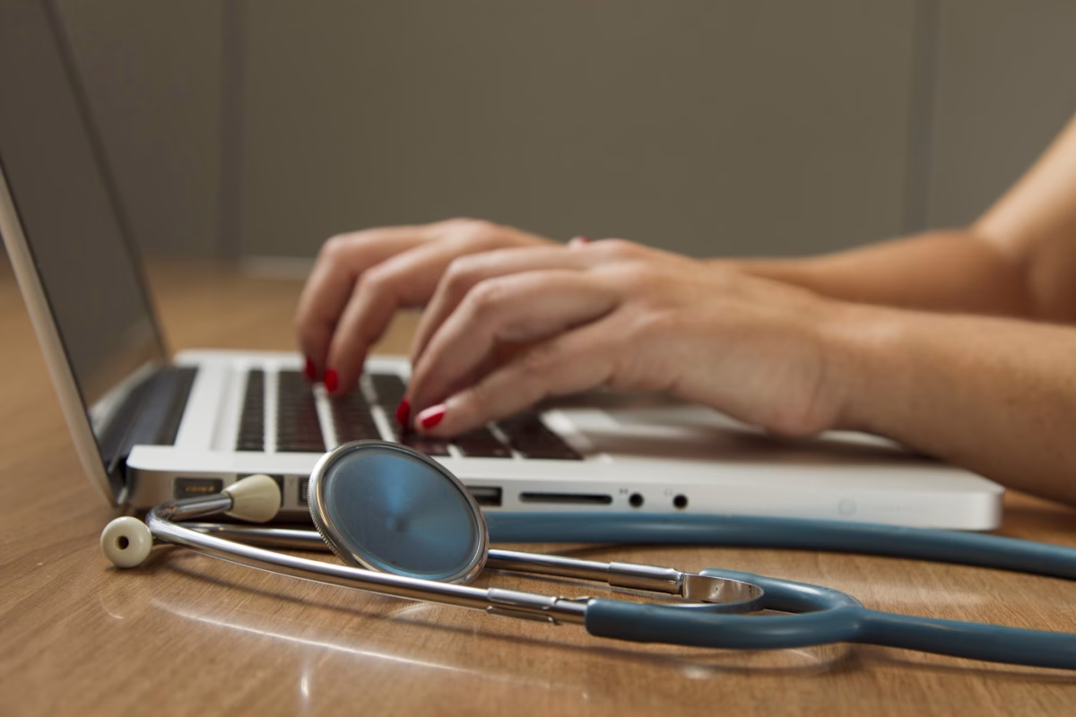 Profesional sanitario usando un ordenador portatil y un estetoscopio en una mesa clinica