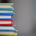 Estudiante usando un portátil con libros y apuntes en una mesa.