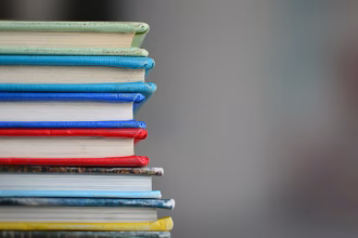 Estudiante usando un portátil con libros y apuntes en una mesa.