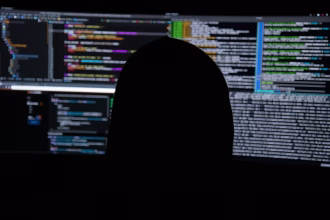 Persona frente a monitores con código, imagen asociada a ciberseguridad y reportes automatizados.